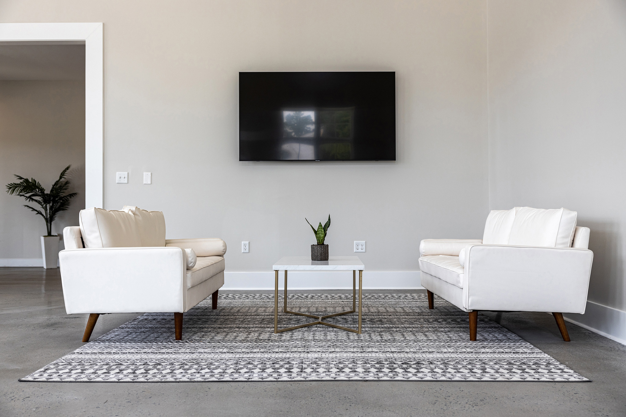 a living room with two white chairs and a television on the wall